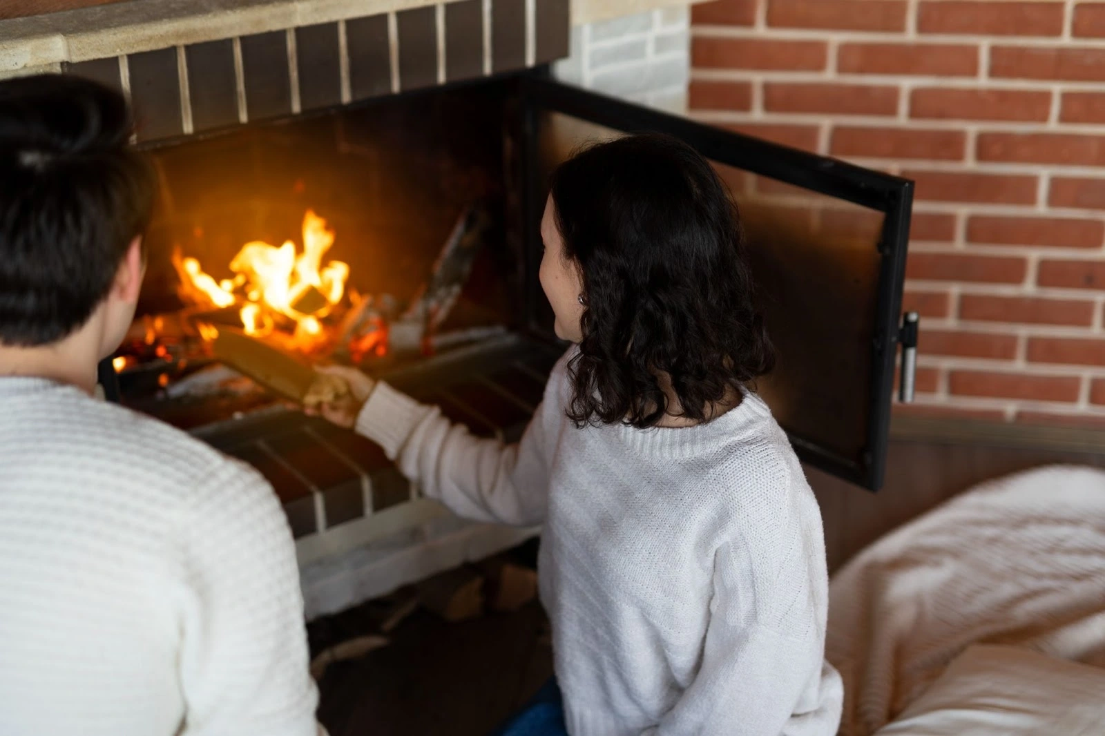 Two people tending a fire in a brick fireplace.