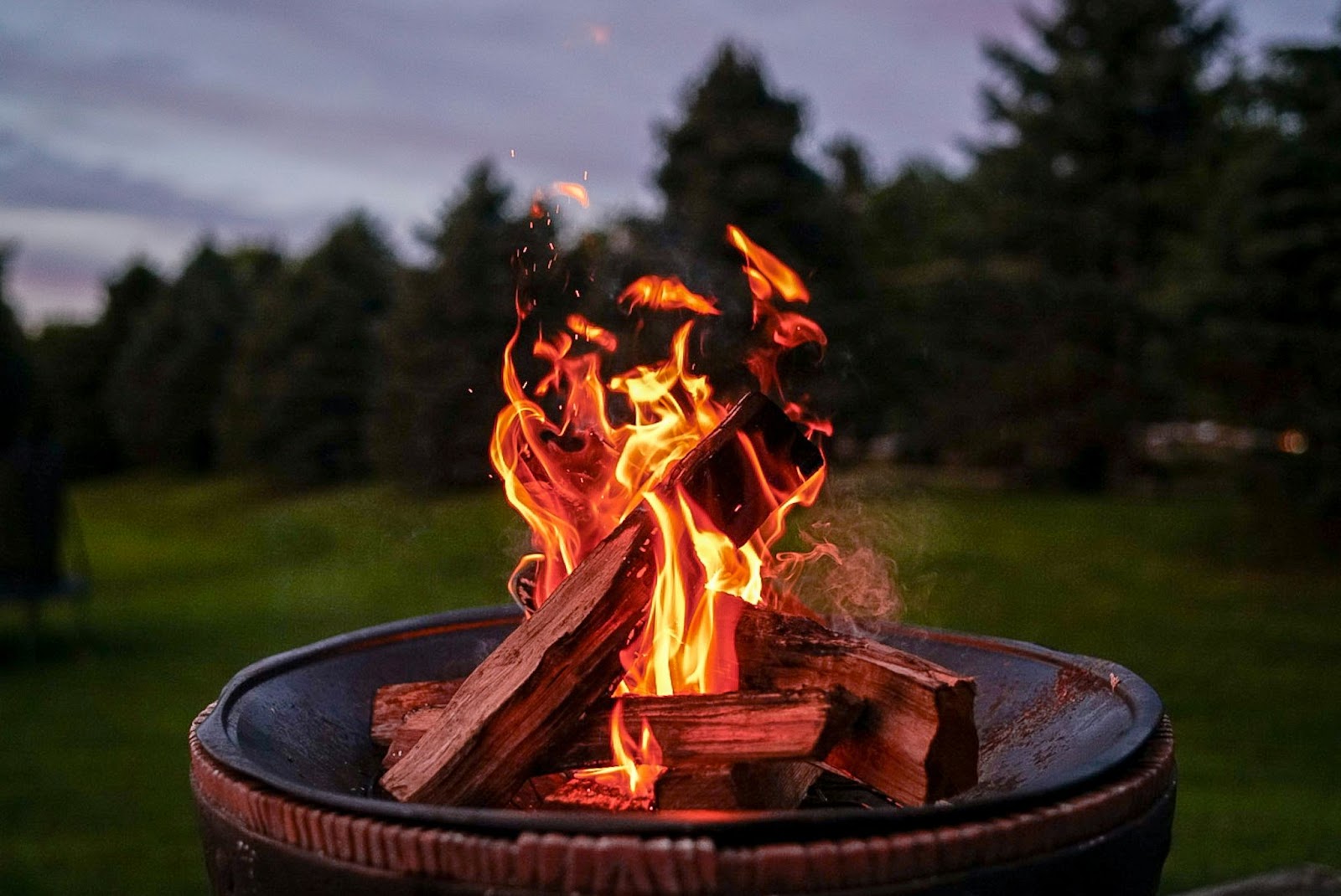 Outdoor fire pit with burning wood logs and visible flames creating a warm ambiance in a backyard setting